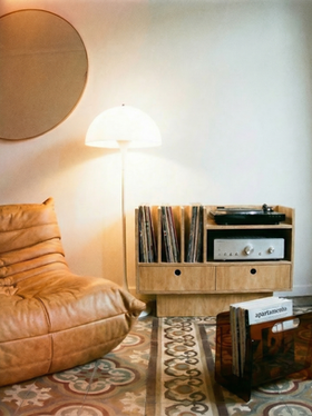 Cozy listening corner with record player stand and vinyl storage, floor lamp and lounge chair in a minimalist room