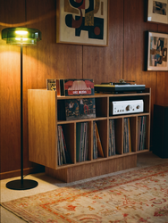 Groove No.3 turntable stand by Groove Wood Studio in birch plywood with a light oak finish, styled with vinyl storage, a receiver, and a turntable beside a floor lamp in a warm wood-paneled room.