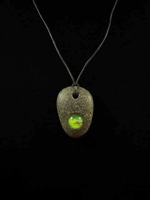 A necklace with a rock pendant that has been hand-carved. Acrylic paint has been placed into the carved circles, then covered with glass. Created by Emilyann Craighead