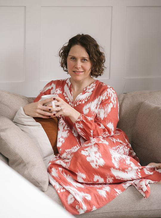 Deoné Duffy seated in an orange and white patterned dress holding a white mug.