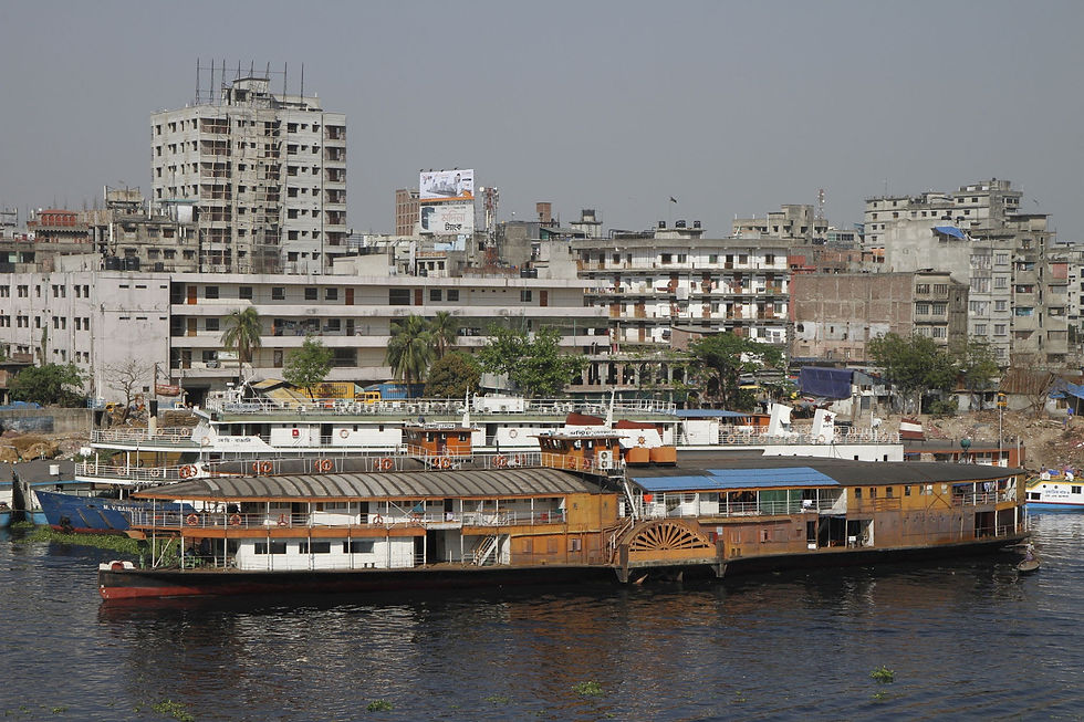 Docked river ferries in front of dense apartment blocks on a hazy city waterfront.
