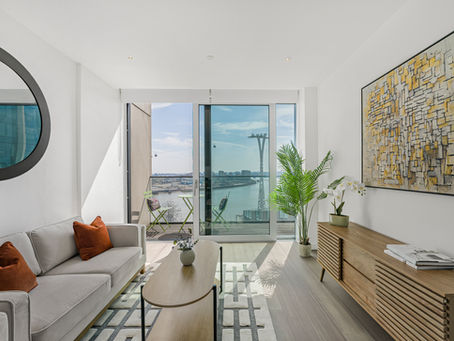 Bright modern living room in a Greenwich Peninsula apartment with floor-to-ceiling windows, balcony views over the River Thames, and stylish contemporary furnishings.