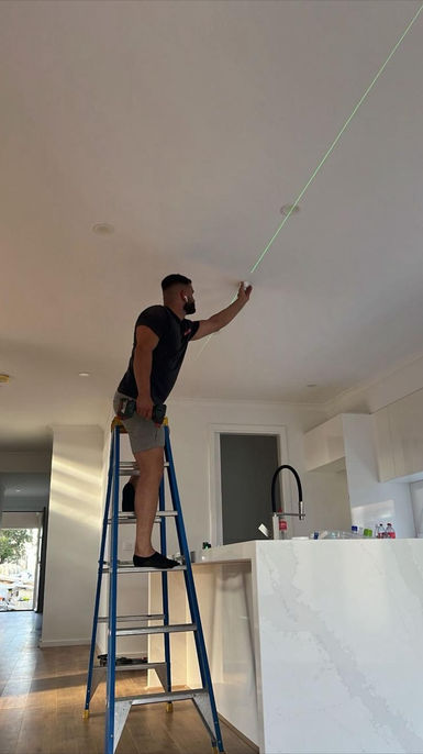 An electrician on a ladder, working on the ceiling wiring of a home.
