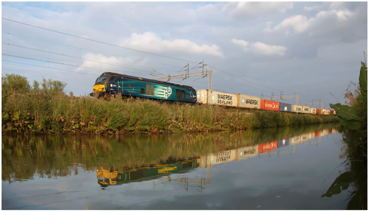 A class 68 passing the oxford canal on a freight liner train with a class 66 reflected in the water.