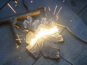 A laser beam cleaning a piece of metal in the shape of a leaf.