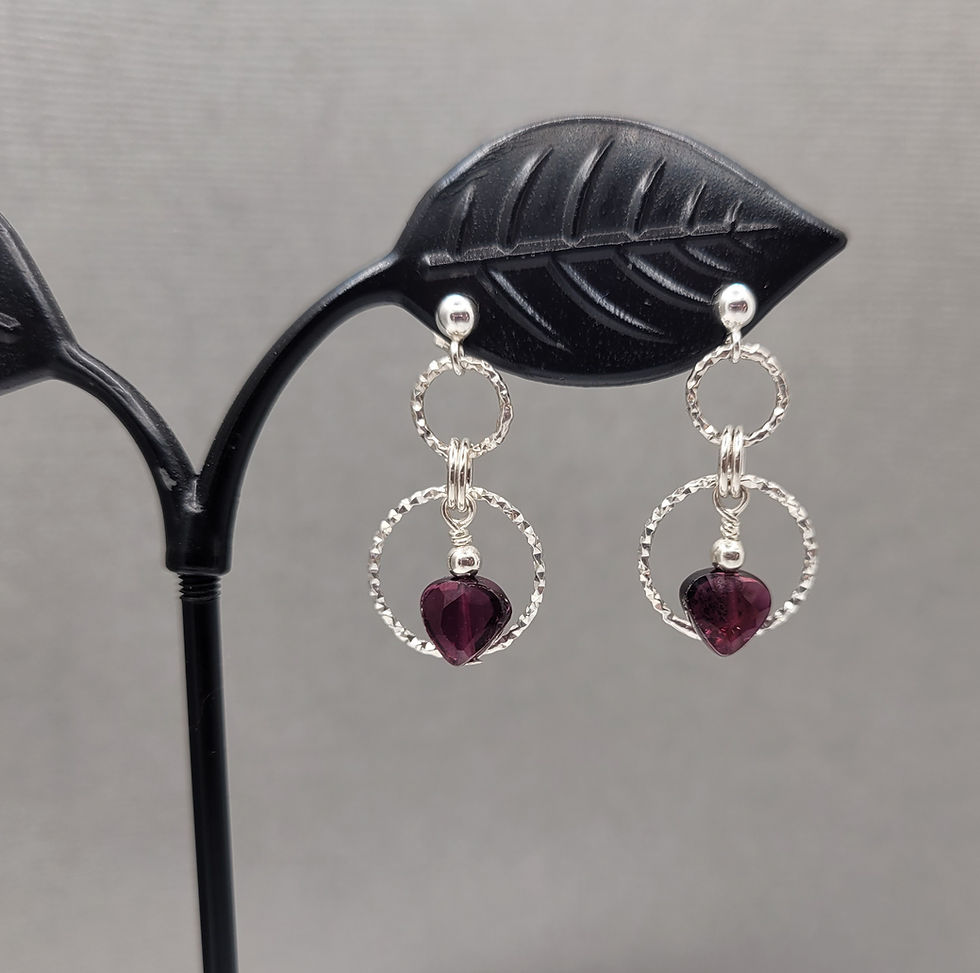 Thumbnail: Garnet bead hanging from decorative sterling silver earrings displayed on black stand