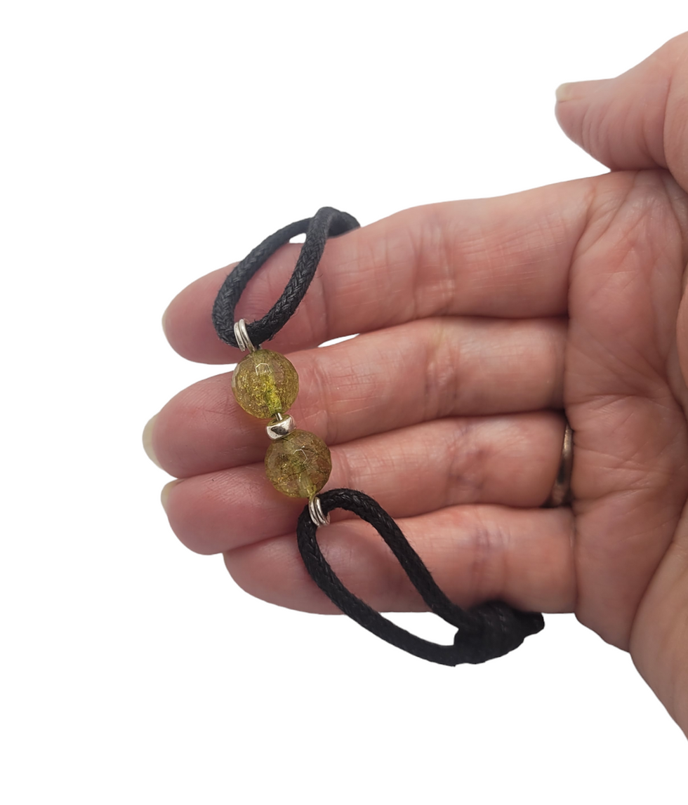 Thumbnail: Hand displaying black cord bracelet with peridot beads