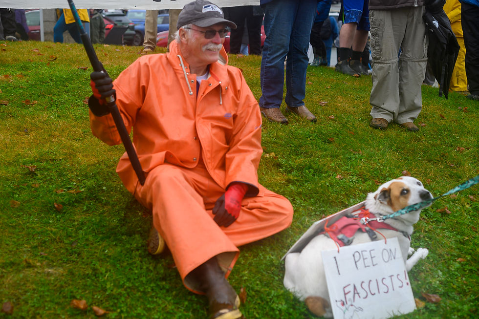 Keith Pahlke sits with his dog, Arya, who wears a sign reading "I Pee on Fascists" during a No Kings rally at Bill Overstreet Park on Saturday, Oct. 18, 2025. (Jasz Garrett / Juneau Independent)