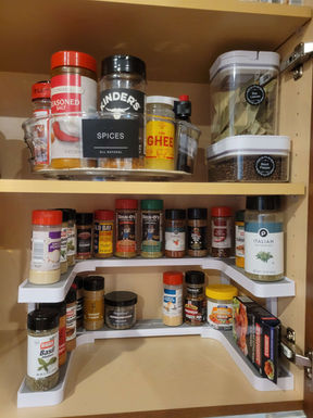 Kitchen spices organized with a tiered spice rack and neatly arranged for easy access along the walls of the cabinet.