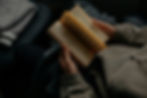 A person wearing a green hoodie and black pants sits and flips through a book.