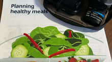 A blood glucose monitor with lancets and test strips on top of a packet detailing how to create a healthy meal.