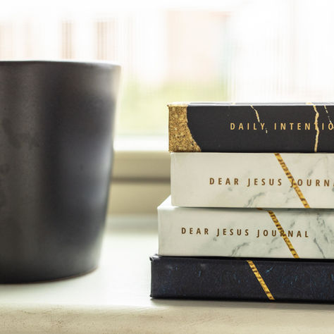 Stacked journals, including the Dear Jesus Journal, beside a pot on a window sill, showcasing journals you can use for your journaling time.