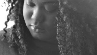 Black and white portrait of writer Kemi Kodja looking down in quiet reflection, capturing a mood of contemplation and surrender.