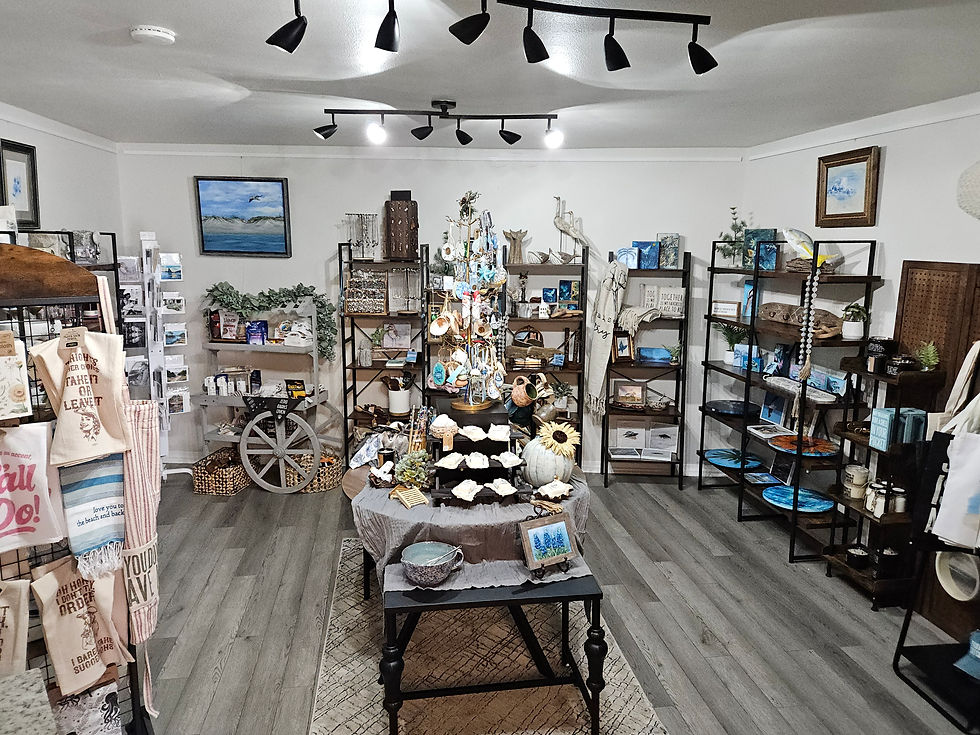 Home décor section of Evoke Studio & Gifts with coastal artwork, shelving displays, a central table of products, and overhead track lighting