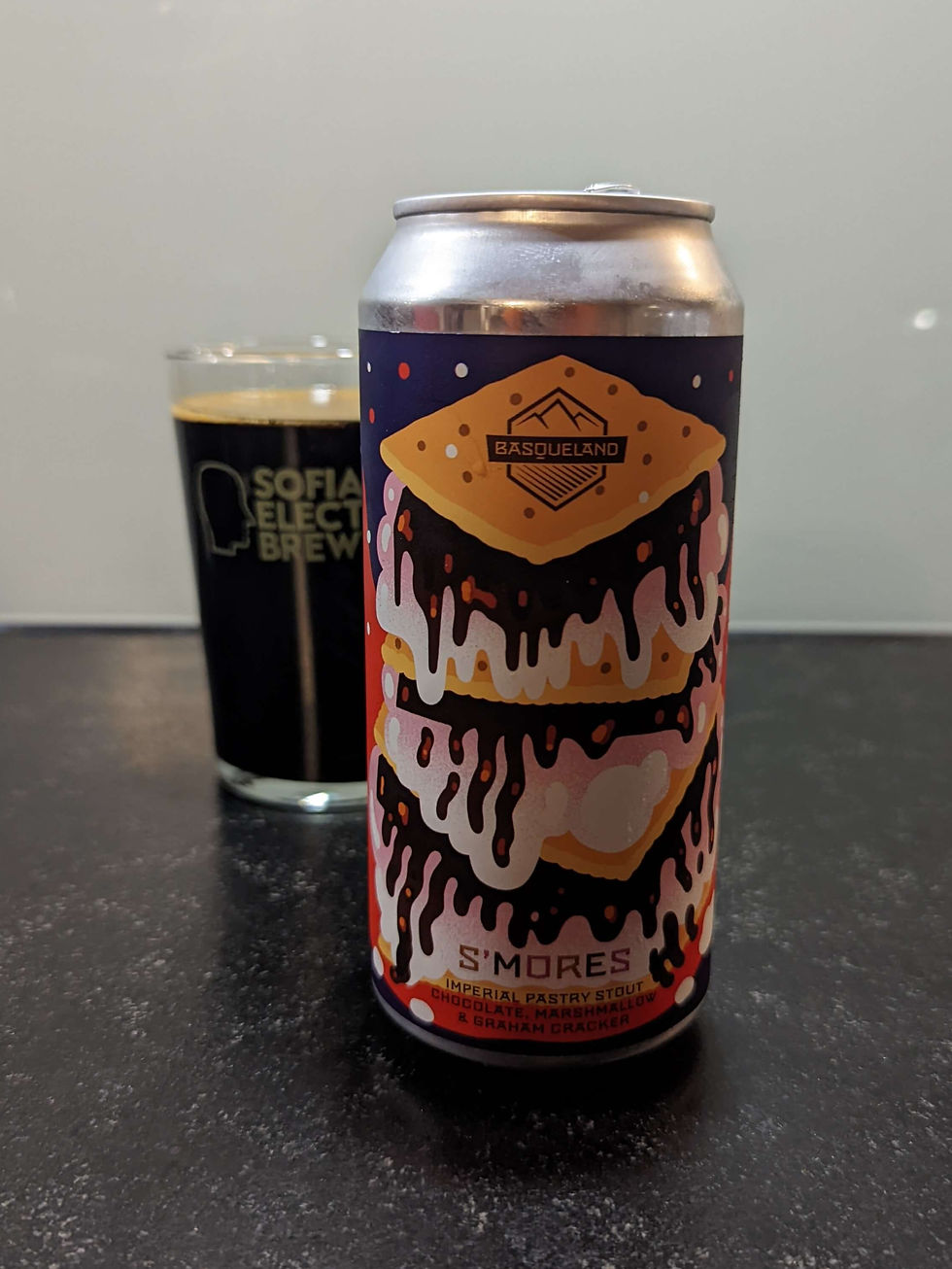 Can of Basqueland S'mores Imperial Pastry Stout with colorful dripping design on a dark countertop. A glass with "Sofia Electric Brewing" in background.