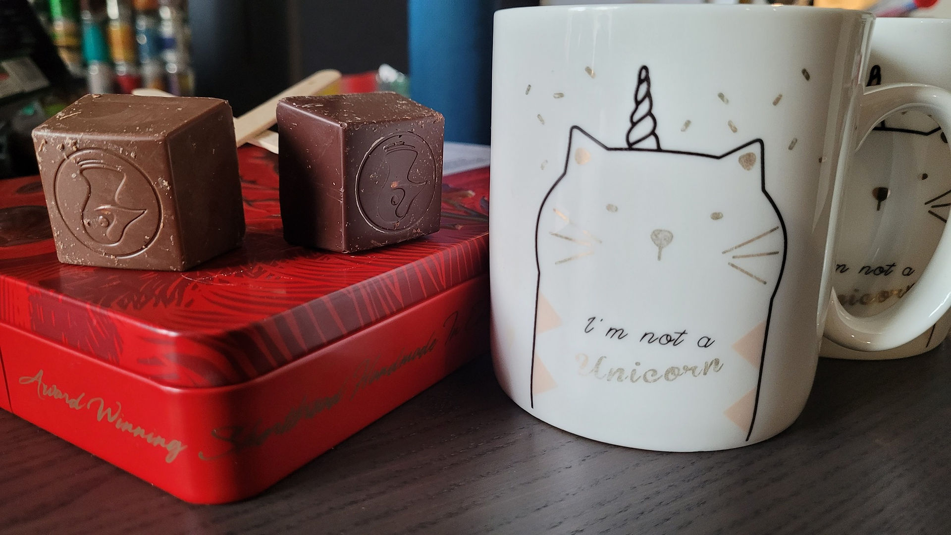 Two Taucherli hot chocolate cubes on a cookie box and a cup of hot milk with a unicorn cat on them