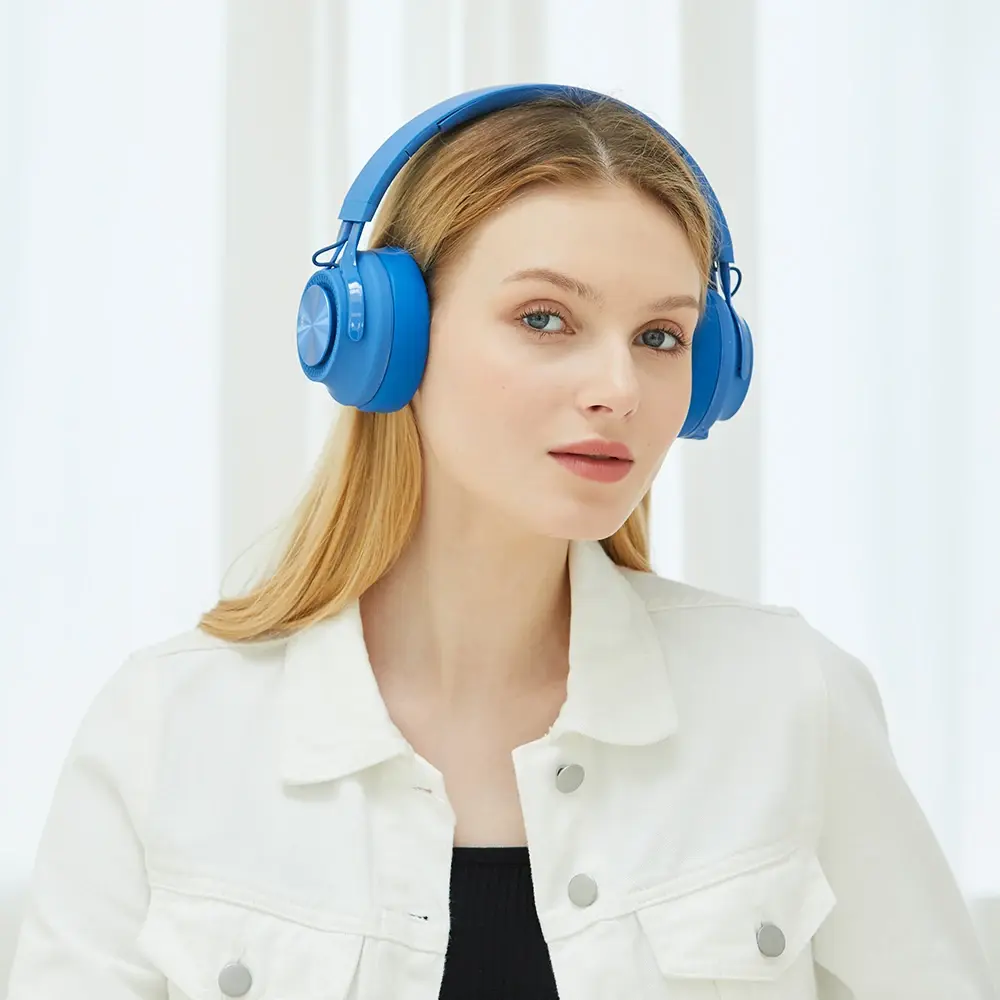 Young woman wearing blue headphones, smiling, indoors with natural daylight.