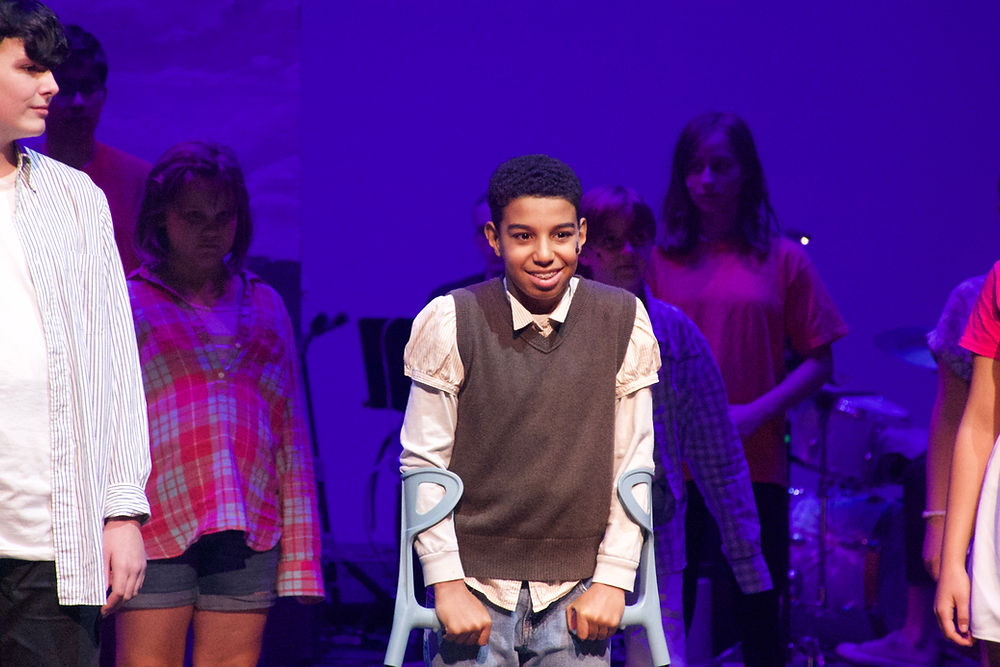 Archie from 13 the Musical, who is on crutches, stands proudly in the middle of a group of classmates