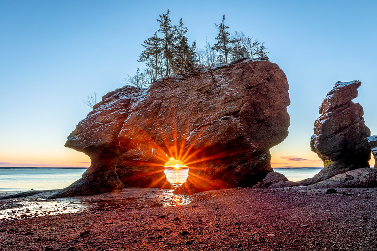 The sun shines through a gap in between two rock formations on the ocean floor at low tide on the Bay of Fundy