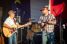 Two musicians on a stage with an Acadian Flag in the background
