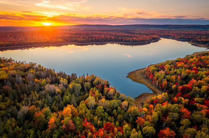 A lake surrounded by trees during the fall, at sunset