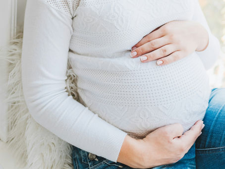 mulher grávida sentada segurando a própria barriga com as duas mãos
