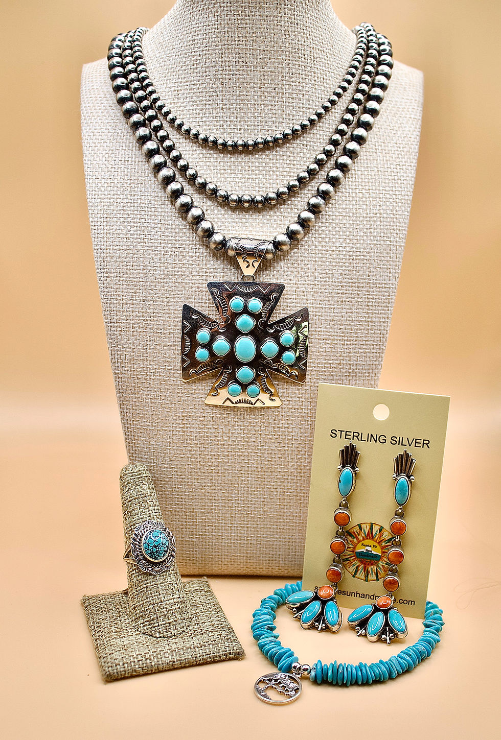 Silver jewelry set with turquoise stones on a tan display. Includes a necklace, earrings, ring, bracelet. Card reads "STERLING SILVER".