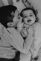 Black and white photo baby and toddler brothers cuddling on bed