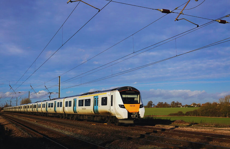Thameslink train travelling through open countryside under overhead power lines.