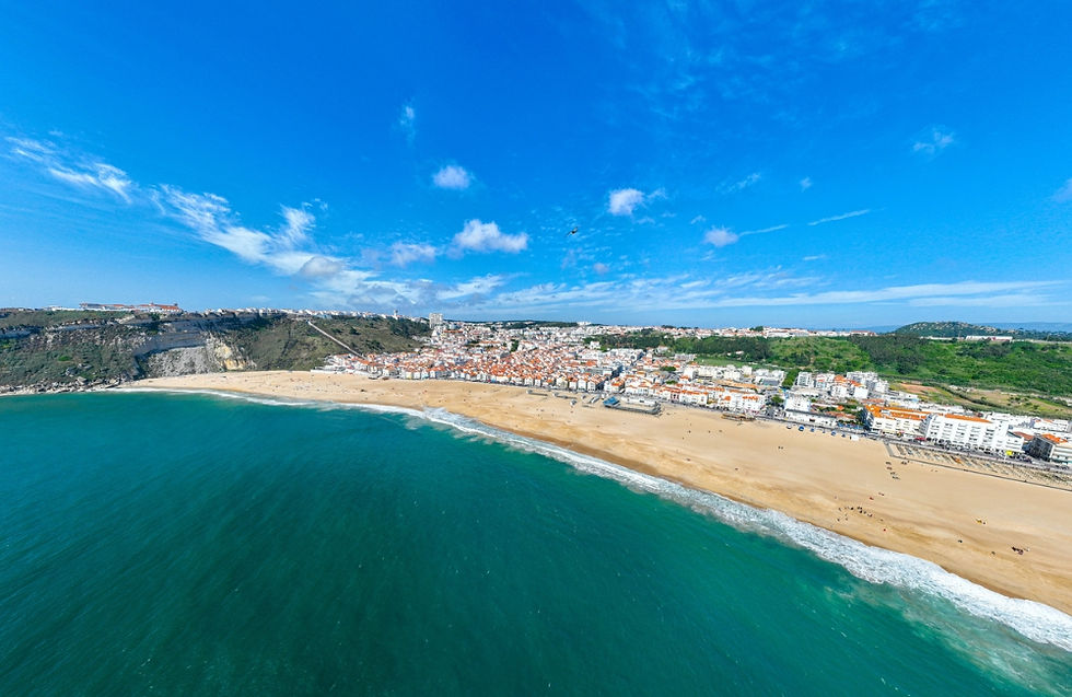 Aerial view of Nazaré beach on the Silver Coast, Portugal, with golden sand, blue ocean, and whitewashed houses.