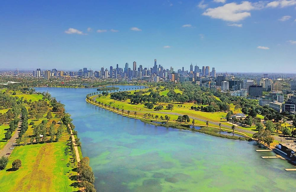 Aerial view of Albert Park Lake and surrounding green spaces with Melbourne city skyline in the background.