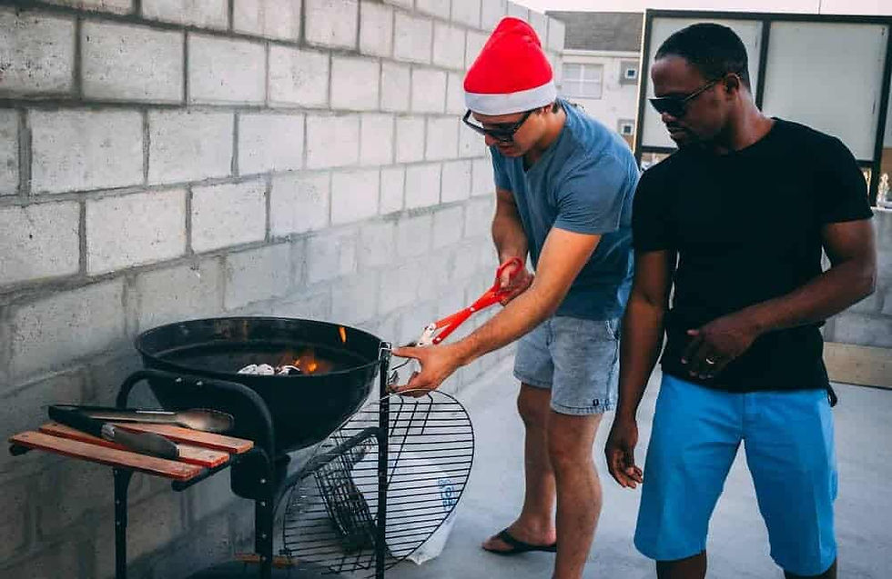 Two people enjoying a festive BBQ outdoors, one wearing a Santa hat while cooking on the grill.