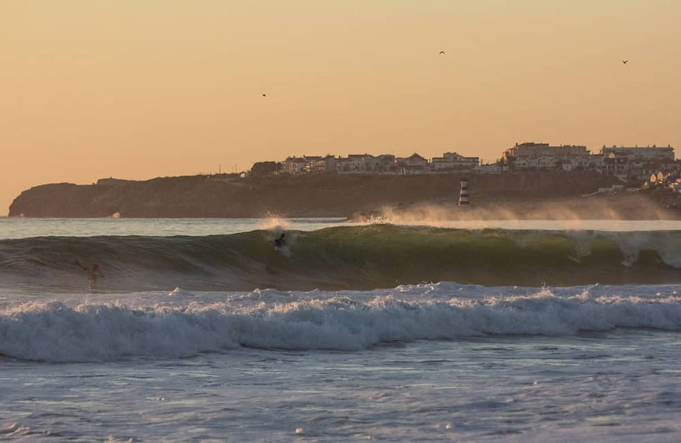 Surfers riding waves at sunset near Peniche, Portugal.
