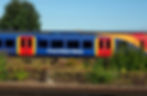 Blue and red South Western Railway train passing greenery on tracks. Clear sky and tree in background, white text visible on train.