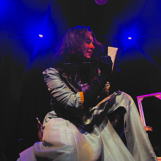 Blue lights frame a hereo-esque figure writing in her notebook with a feather pen.