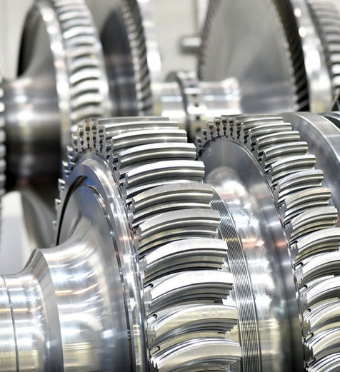 Extreme close-up of multiple shiny, precision-machined rotor wheels discs with integral blades, likely part of an axial compressor or steam/gas turbine rotor. The metallic surface is highly reflective, showing the complex, stepped stages and blade profiles in sharp detail, suggesting a component for high-performance turbomachinery.