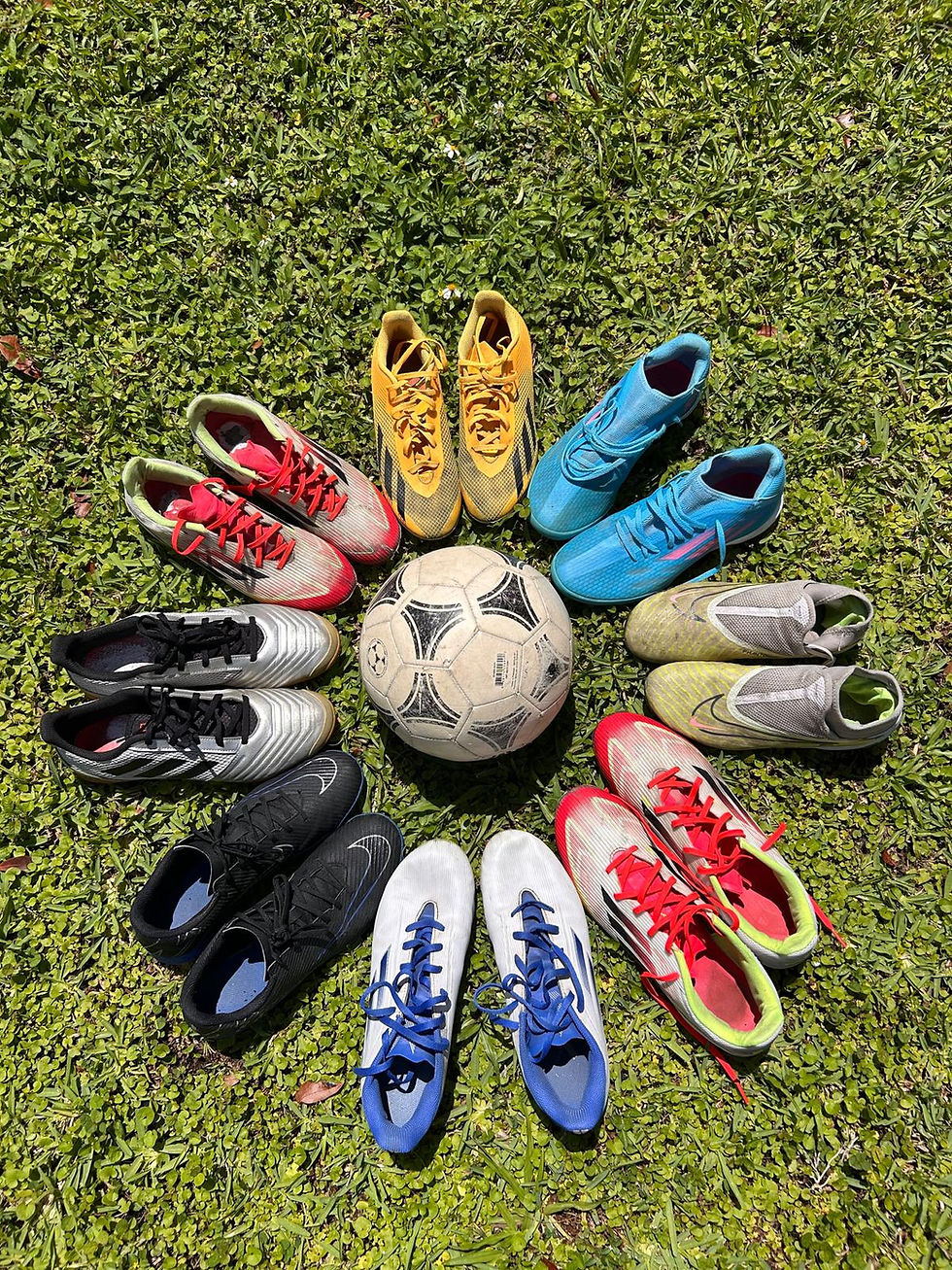 Multiple colorful soccer cleats arranged in a circle around a worn soccer ball on green grass, collected by ToesUp for donation to underprivileged children