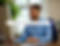 Man in blue shirt working at desk, smiling at computer. Text overlay reads: "Why Every Busy Entrepreneur Needs a Dedicated Virtual Assistant." Bright office with plants.