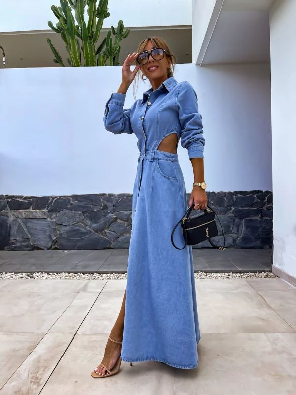 Woman wearing a long-sleeve, button-down denim maxi dress with side cut-outs and a high slit, styled with black heels, sungla