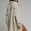 Thumbnail: Woman wearing an oversized stone-colored cotton gauze shirt dress over a black bralette and denim shorts, back view