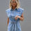 Thumbnail: Model styling The Dakota Denim Romper with white cowboy boots, sunglasses, and a white handbag – bold and Western-chic look.”