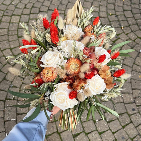 Bouquet de mariée en fleurs séchées et lyophilisées dans des tons rouges, orangés et blancs.