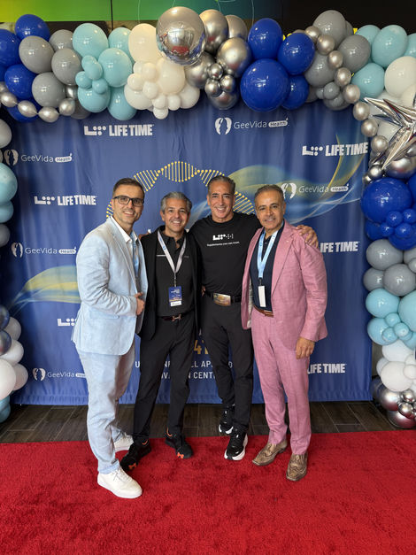 Four men pose together in front of a blue backdrop with logo.