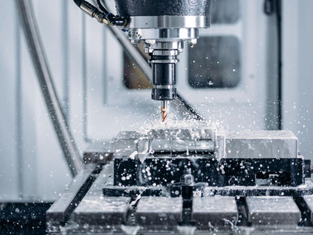 CNC milling machine drilling a metal block, coolant spraying in a bright industrial workshop.