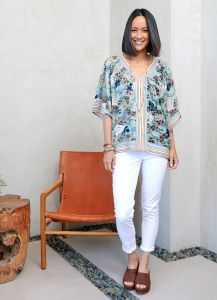 Woman wearing a floral V-neck blouse with white skinny jeans and brown woven slide sandals.