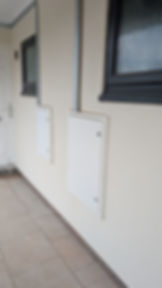 Bespoke white meter access panels installed on a building exterior, secured with visible fixing screws.