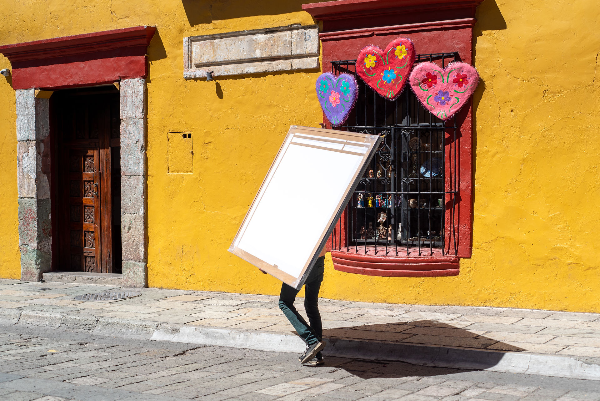 Mexican Oaxaca street bright vivid yellow building with colourful heart decor and a anonymous person walking a big art canvas