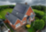 Brick house with gray roof solar panels in heavy rain, surrounded by lush green hedges and lawn under dark storm clouds