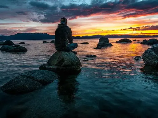 A man sitting on a rock in a lake at sunrise