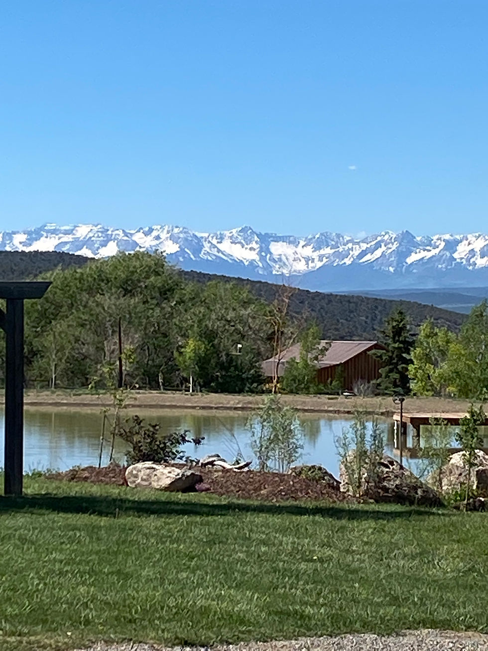 Spring snowcapped mountains and peaceful pond with barn in the background at one of Colorado's barn wedding venues